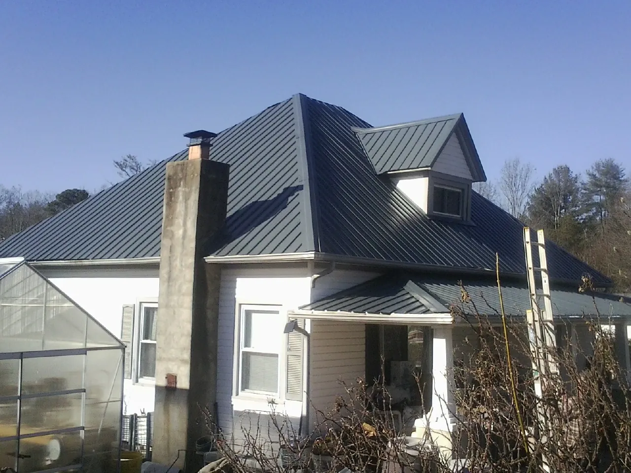 Dark blue standing seam metal roof on a white farmhouse with dormer — Slate & Tile Roof Repair by Roofing Brothers in Shevlin