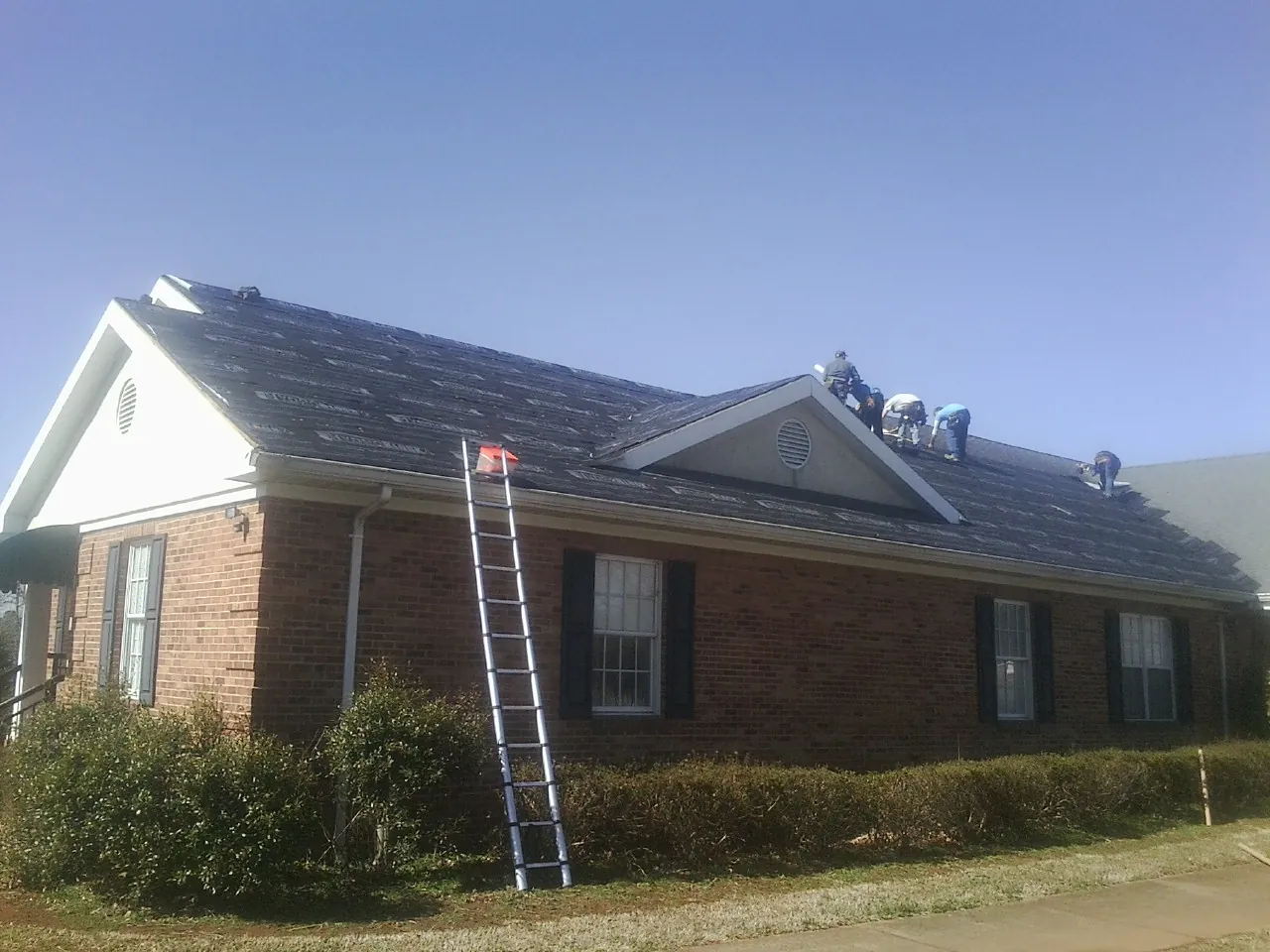Crew tearing shingles off a brick ranch roof with a ladder set — Emergency Roof Repair work by our crew in Shevlin