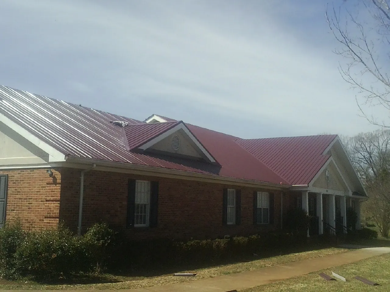 Red metal roof with gabled entries on a long brick building, from a Hail Damage Roof Repair job in Shevlin