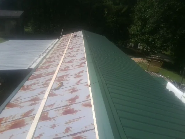 Old rusted panels beside newly installed green metal roofing — Wind Damage Roof Repair by Roofing Brothers in Shevlin