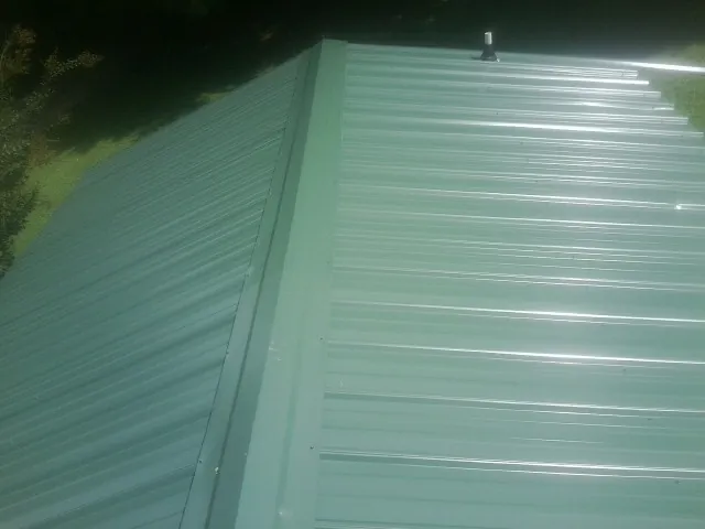 New green metal panels meeting at the ridge of a roof — Flat Roof Repair work by our crew in Shevlin