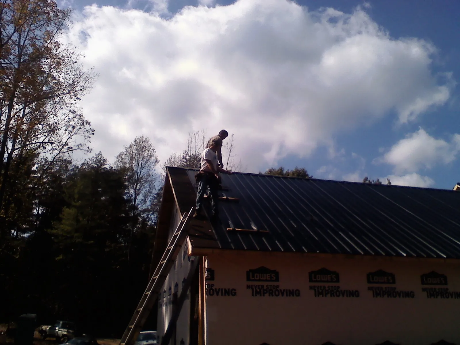 Roofer fastening dark metal panels high against a cloudy sky, from a Roof Inspection job in Shevlin