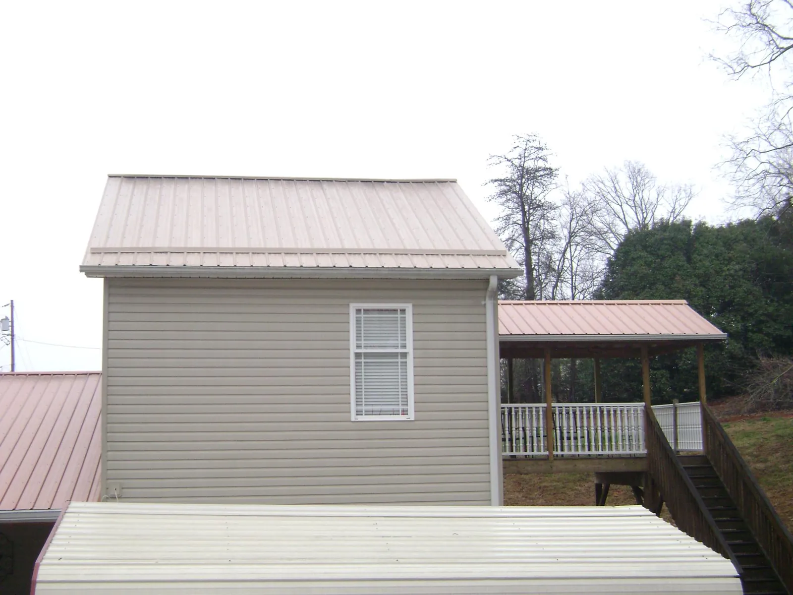 Tan metal roofs on a two story addition and attached porch, from a Roof Replacement job in Shevlin